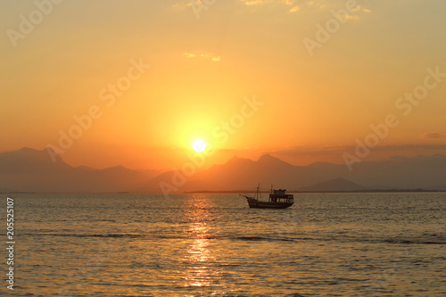 Barco passando enquanto o Sol se põe entre as montanhas © Adriane