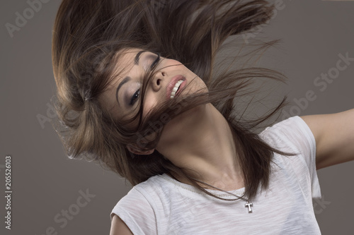 Stopped motion of beautiful young straight hair brunette tossing hair and looking at camera over gray studio background. 