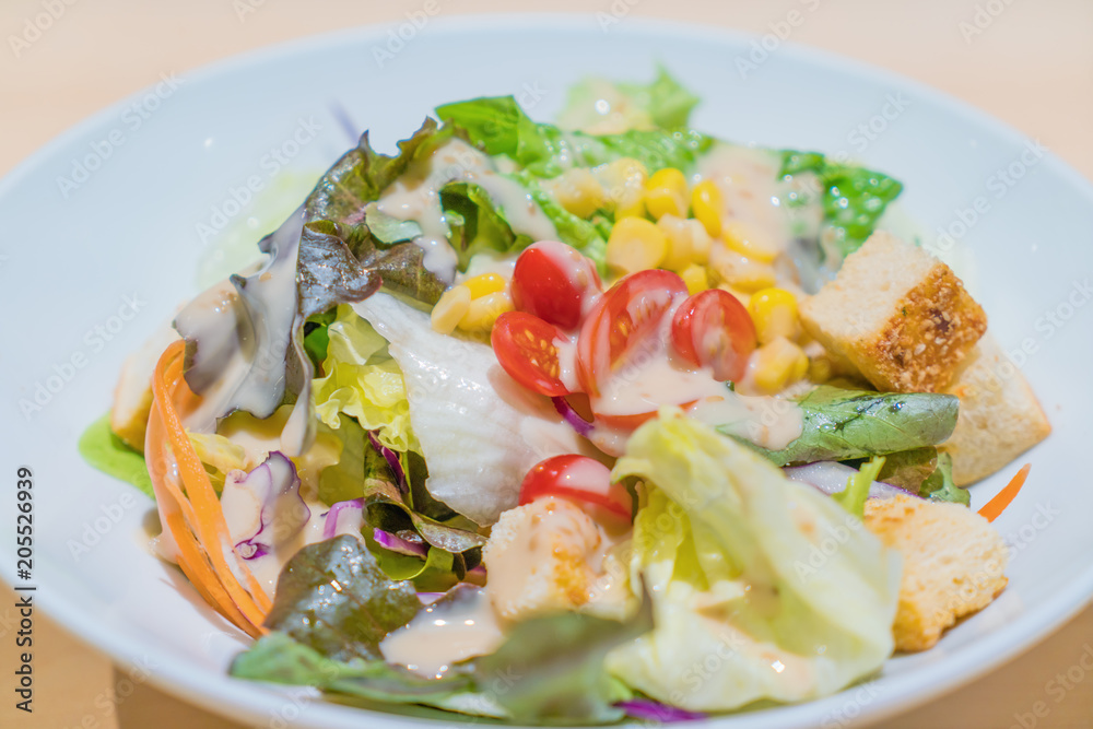 Fresh salad with chicken, tomatoes and mixed greens (arugula, mesclun, mache) in white bowl on wooden table. Healthy food..