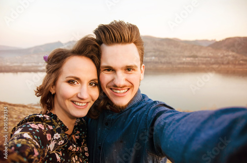 Couple in love do selfie on hills and river background.