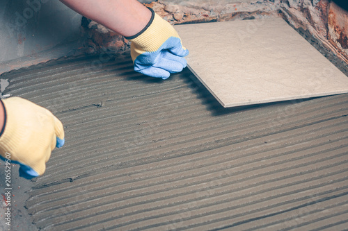 The tiler puts his hands in yellow gloves square tile on the floor