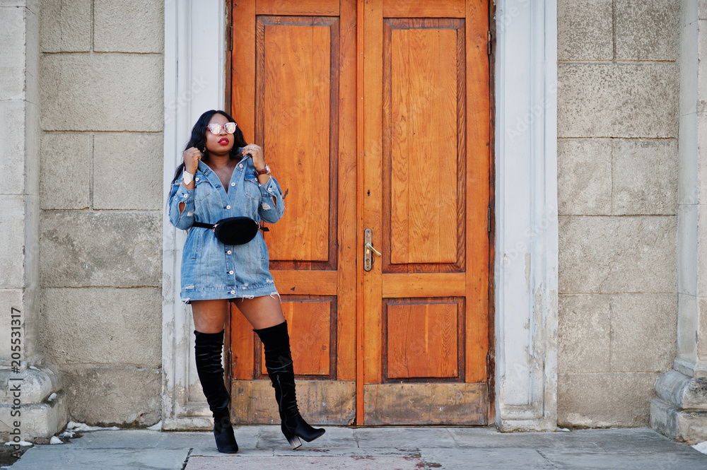 African american girl in jeans dress and sunglasses posed on streets of city. Black stylish model shoot. African american girl in jeans dress and sunglasses posed on streets of city. Black stylish model shoot.