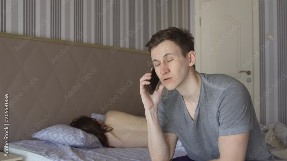 Man is sitting on the bed with a phone on the background of a naked woman. Man is sitting on the bed with a phone on the background of a naked woman.