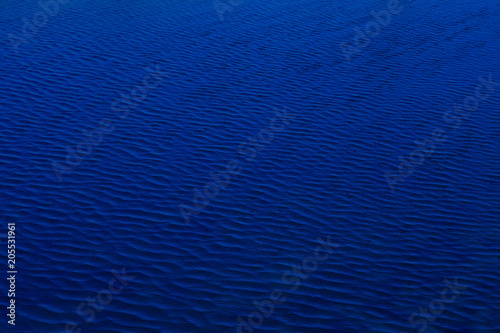 The dark shadow blue water surface has waves pattern for use as background and texture.