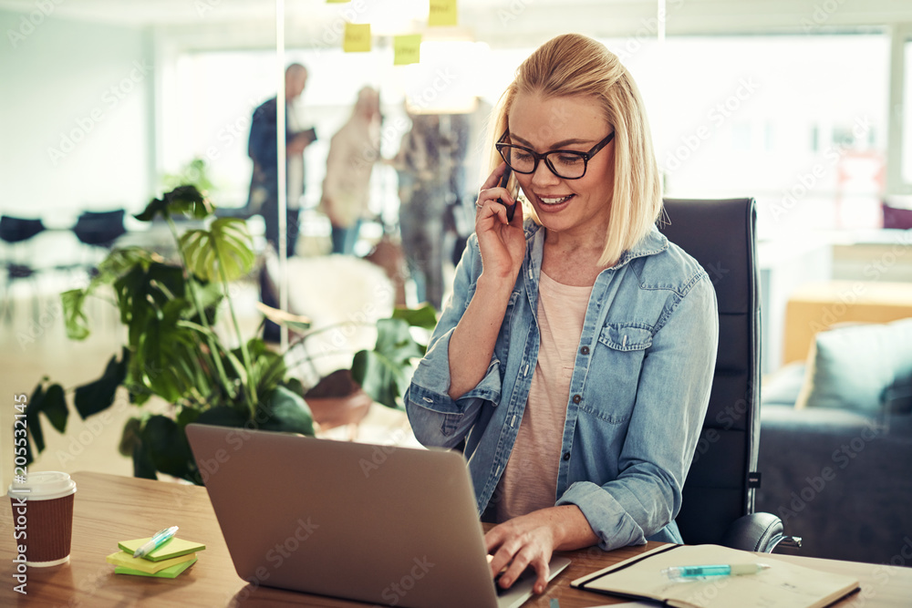 Obraz premium Smiling young businesswoman talking on a cellphone at her desk