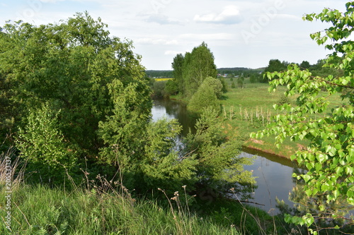 spring landscape, river flowing, green trees, bushes, grass, sky with clouds