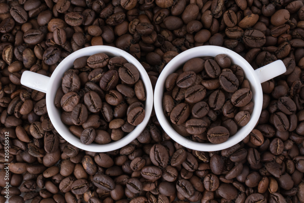 Two white cups with coffee beans on the background of coffee beans