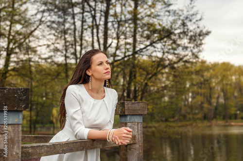 Slika na platnu dreaming pensive young woman stands leaning on a railing of a wooden bridge in a