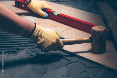 The working tiler knocks on the tile with a Tile Mallet, the professional checks the building level
