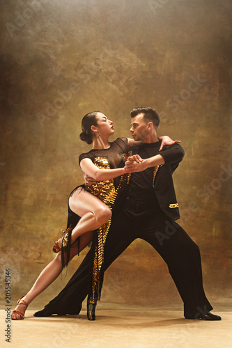 Dance ballroom couple in gold dress dancing on studio background.