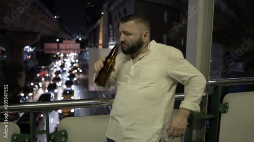 Drunk man walking on the balcony above the road and drinking beer 
 photo