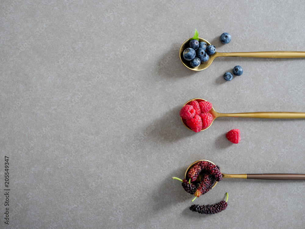 mulberry, blueberries and raspberries, served on spoons on a gray background mulberry, blueberries and raspberries, served on spoons on a gray background