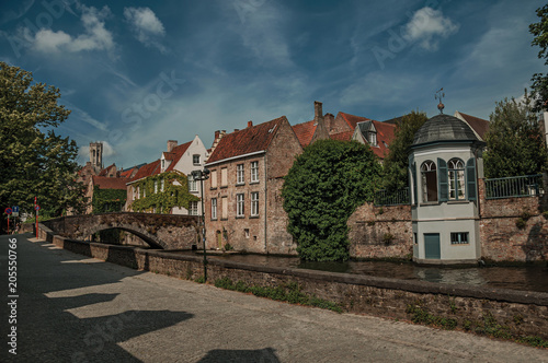 Bridge, trees and brick buildings on the canal's edge in a sunny day at Bruges. With many canals and old buildings, this graceful town is a World Heritage Site of Unesco. Northwestern Belgium.