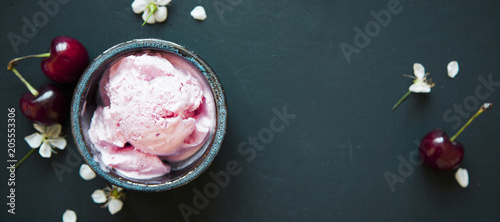 Cherry ice cream scoop in bowl, fresh cherry berries and flowers on dark green background.