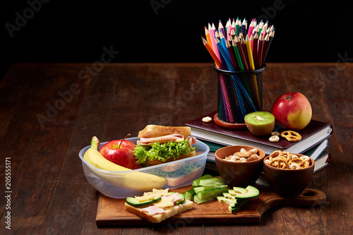 Concept of school lunch break with healthy lunch box and school supplies on wooden desk, selective focus.