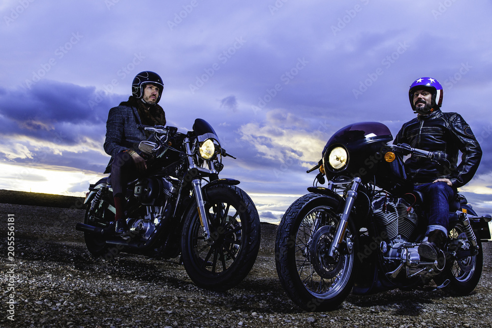 Modern bikers sits and talks on classic motorcycle at sunset. Outdoor portrait and urban lifestyle
