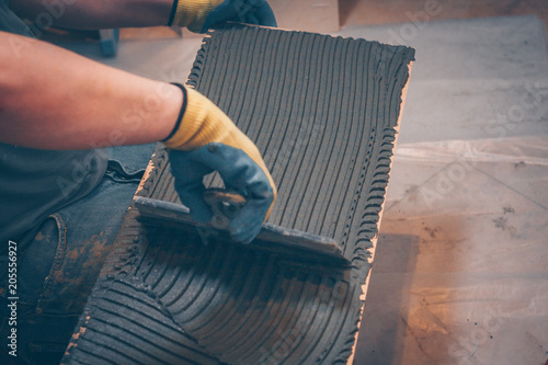 Fotografi The working tiler applies glue on the tile with a notched trowel before gluing,