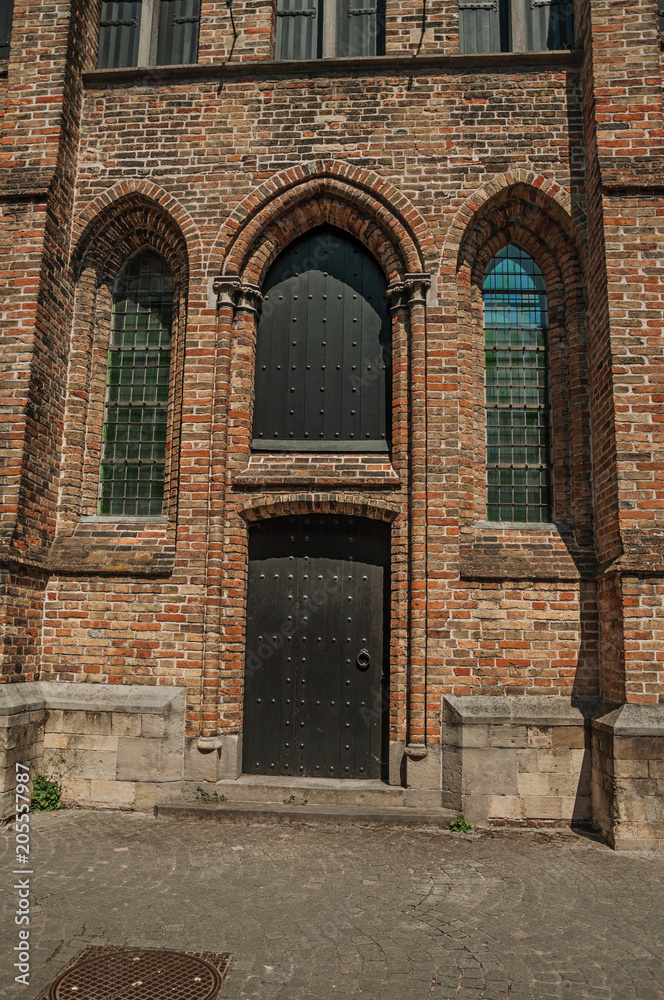 Wooden gate and windows on Gothic church under a sunny day, in an alley of Bruges. With many canals and old buildings, this graceful town is a World Heritage Site of Unesco. Northwestern Belgium.