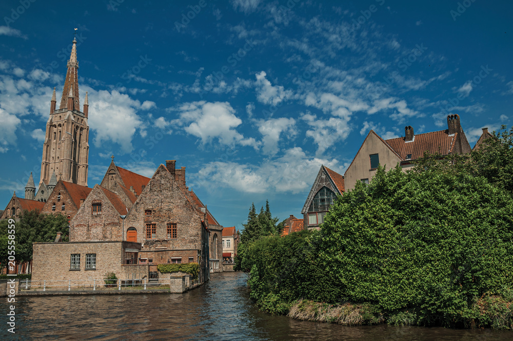 Steeple and old brick buildings on the canal's edge in a sunny day at Bruges. With many canals and old buildings, this graceful town is a World Heritage Site of Unesco. Northwestern Belgium.