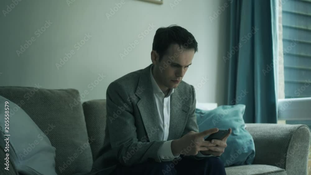 Business Man texting on phone remotely bored sedentry. Handheld shot of business man sitting on sofa texting, looking slightly bored. Business Man texting on phone remotely bored sedentry. Handheld shot of business man sitting on sofa texting, looking slightly bored.