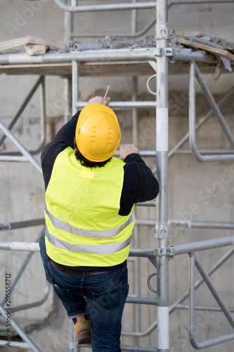 Back turned construction worker climbing a ladder up to the scaffolding