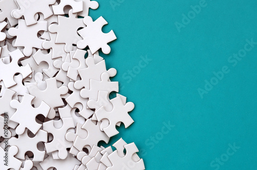 A pile of uncombed elements of a white jigsaw puzzle lies on the background of a blue surface. Texture photo with copy space for text