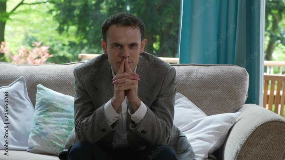 Slow Dollly of Man Thinking Intently on the Sofa. Slow pan on young entrepreneur deep in thought staring pensively into camera