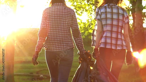 two girls volunteers shirts at sunset with garbage