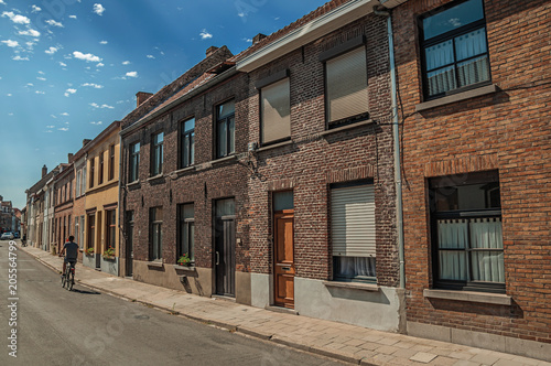 Cyclist and brick facade of old houses with a sunny blue sky in a street of Bruges. With many canals and old buildings, this graceful town is a World Heritage Site of Unesco. Northwestern Belgium.