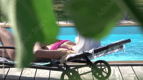 POV: Stalker spying and filming an unaware girl sun tanning in a pink bikini from behind a bush. Crazy next door neighbor taking photos of attractive Caucasian woman sleeping by herself near the pool.