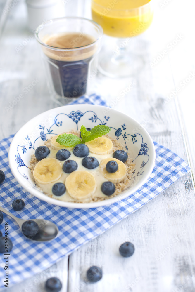 Delicious and healthy breakfast. Oatmeal with berries, aromatic coffee and fresh orange juice. White wooden background and blue napkin. Good morning Delicious and healthy breakfast. Oatmeal with berries, aromatic coffee and fresh orange juice. White wooden background and blue napkin. Good morning