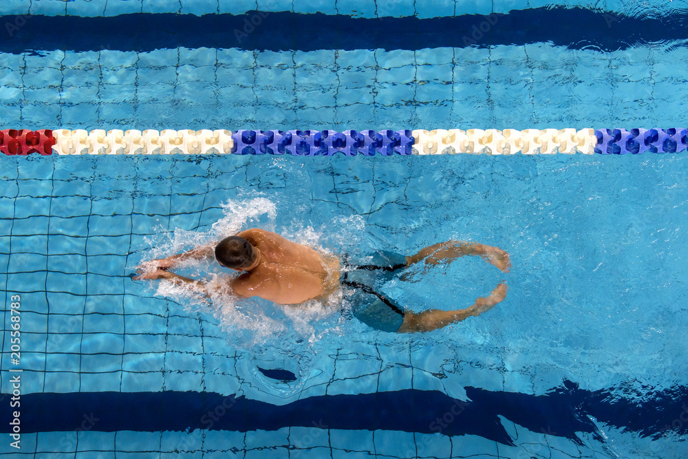 YOUNG MALE SWIMMER EXERCISING FREESTYLE SWIMMING IN POOL LANE LINE , WATER SPLASHING
