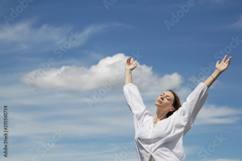 Young woman in white shirt with raised hands and fluffy sky background