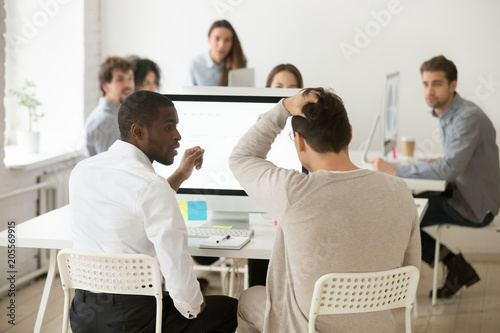 Rear view of stressed businessman suddenly realized problem mistake using pc with colleague in office  diverse team looking at frustrated coworker shocked by bad news online or unexpected dismissal