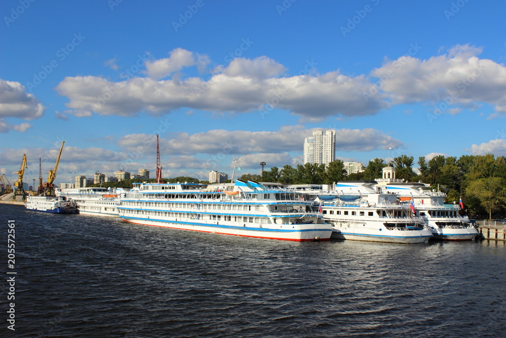 Three cruise ships at the pier of the Northern river port in Moscow on the background of port cranes and blue summer sky with clouds