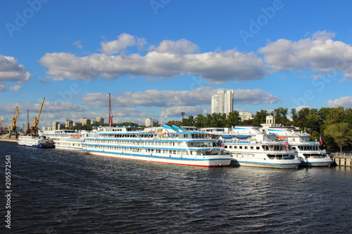 Three cruise ships at the pier of the Northern river port in Moscow on the background of port cranes and blue summer sky with clouds © Ilya