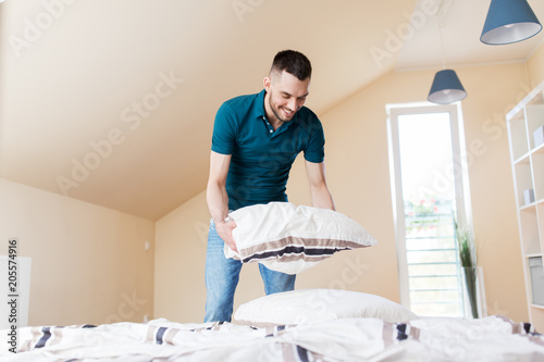 household, housework and cleaning concept - happy man making bed at home