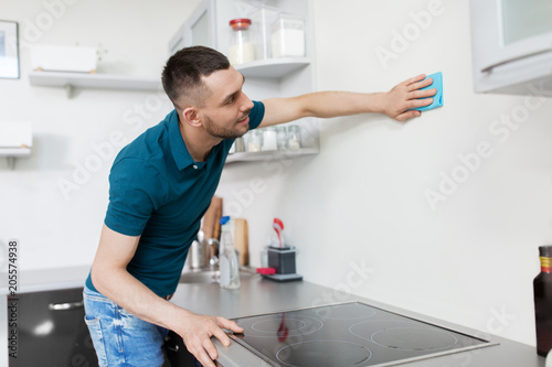 household and people concept - man with cloth cleaning wall at home kitchen