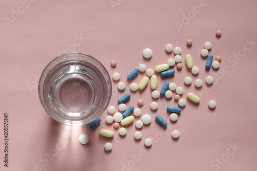Overhead view of medicines with drinking water in glass over coral background photo