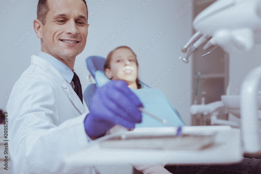 Working process. Cheerful male dentist smiling while carrying mouth mirror