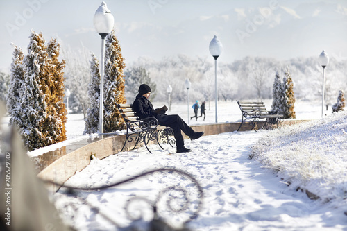 Man reading book while sitting on park bench during winter photo