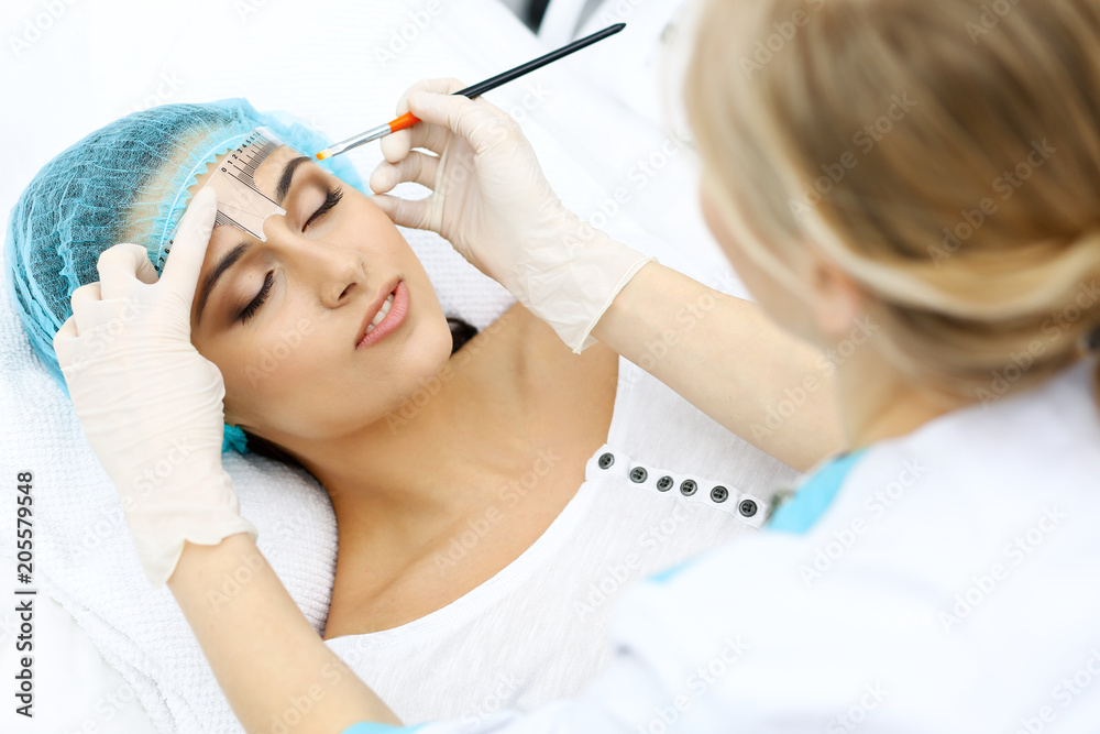 Professional beautician is going to correct eyebrow line at woman face using cosmetic ruler. Permanent brow makeup in beauty salon, closeup. Cosmetology treatment Professional beautician is going to correct eyebrow line at woman face using cosmetic ruler. Permanent brow makeup in beauty salon, closeup. Cosmetology treatment