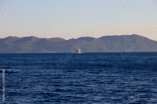 Widok z lądu na spokojnych wodach Morza Śródziemnego w Chorwacji. Na horyzoncie prom wracający z wyspy Mljet.