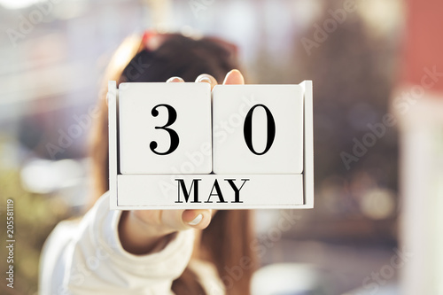 the woman is holding a white wooden calendar. White wooden cube shape calendar for MAY 30 with hand 