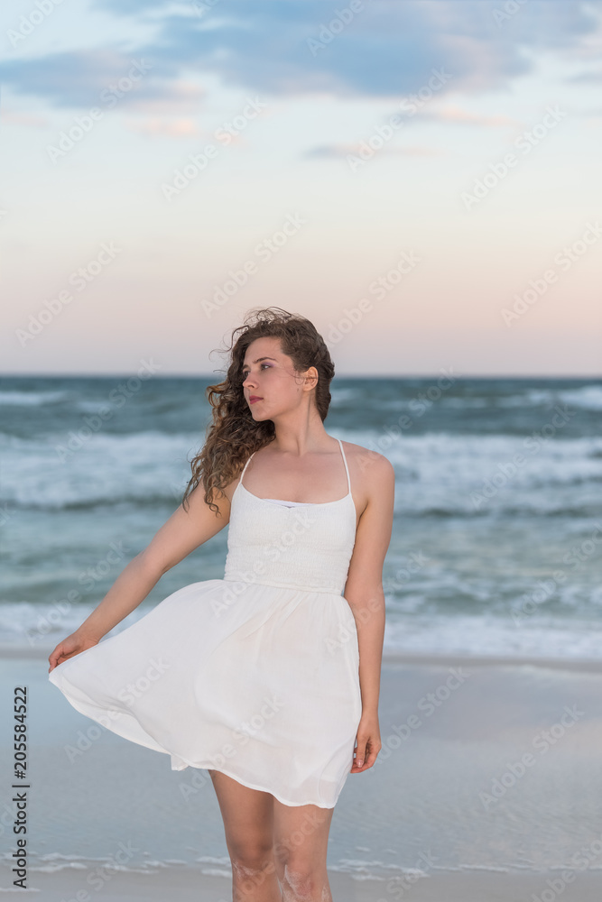 Young woman in white dress on beach sunset in Florida panhandle with wind, ocean waves, side profile looking away Young woman in white dress on beach sunset in Florida panhandle with wind, ocean waves, side profile looking away
