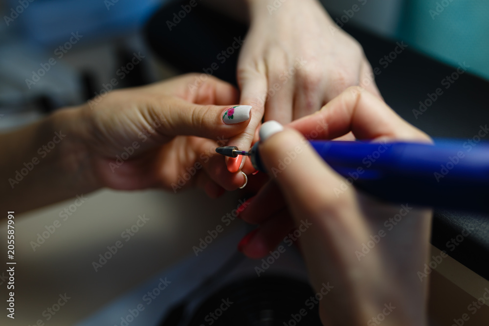 Closeup shot of hardware manicure in a beauty salon. Manicurist is applying electric nail file drill to manicure on female fingers. Manicurist takes off the manicure shellac with a nail client.