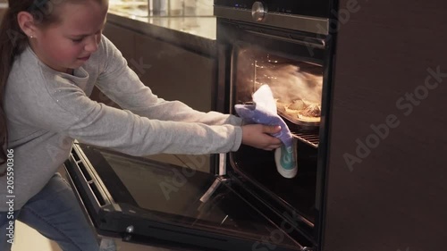 Girl opens oven and takes burnt cookies, smoke from overcooked food is coming