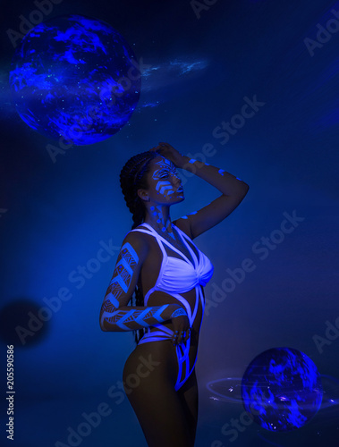 The girl is an alien, the sexual keeper of the universe is walking among the galaxies against the background of the planets. Art on the body fluorescent paints. Photosession with ultraviolet light.