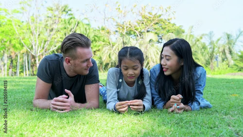 Family in park relaxing. Young family laying down on grass talking to each other, relaxing. White man, chinese woman, chinese girl. Mixed raced family concept. Family in park relaxing. Young family laying down on grass talking to each other, relaxing. White man, chinese woman, chinese girl. Mixed raced family concept.