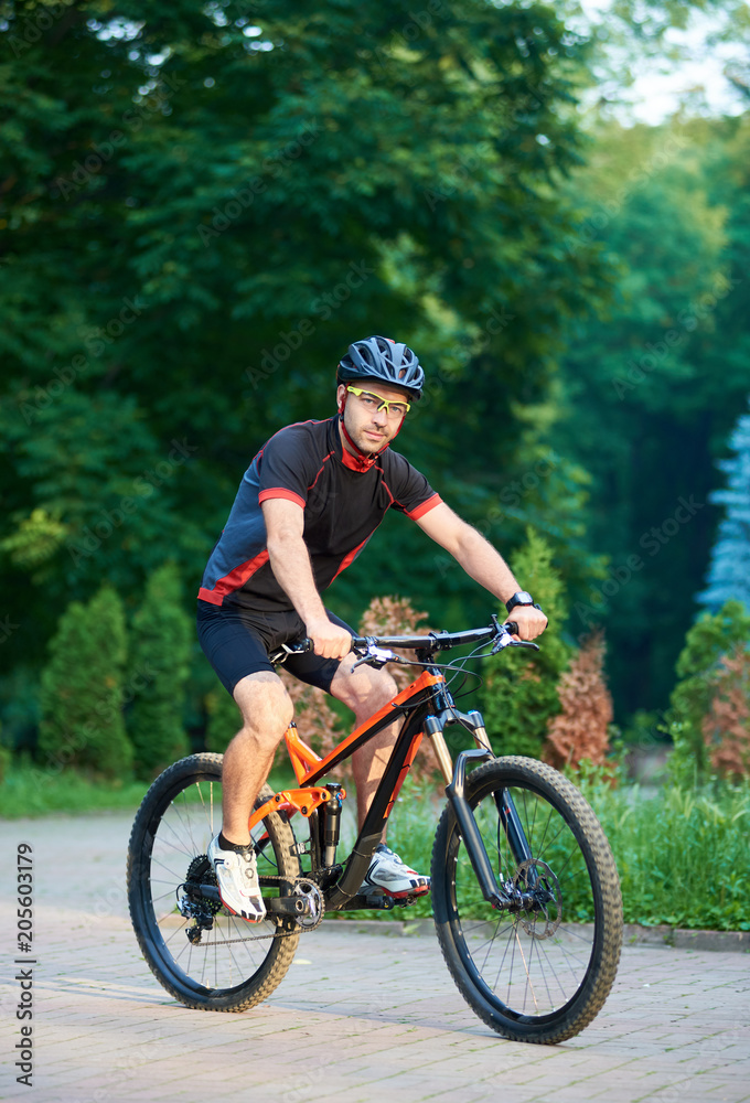 Sporty man bicyclist riding on professional bicycle, training paved park alley. Muscle sportsman getting ready for contest. Cycler shooting for cycling garment ad. Concept of healthy lifestyle